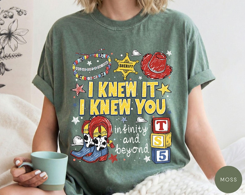 May include: A moss green short-sleeve t-shirt featuring a graphic print with a sheriff badge, a red cowboy hat, a beaded bracelet, cowboy boots, and alphabet blocks. The text reads I KNEW IT I KNEW YOU infinity and beyond.