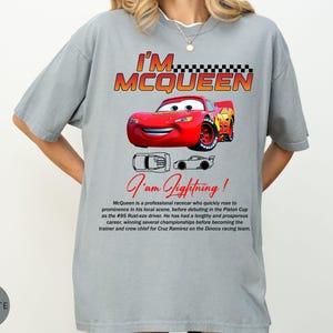 Puede incluir: Camiseta gris con un coche de carreras de dibujos animados rojo y el texto "I'M MCQUEEN". Debajo del coche, el texto "I am Lightning!" est&aacute; escrito en cursiva. La camiseta tambi&eacute;n tiene una descripci&oacute;n del coche.