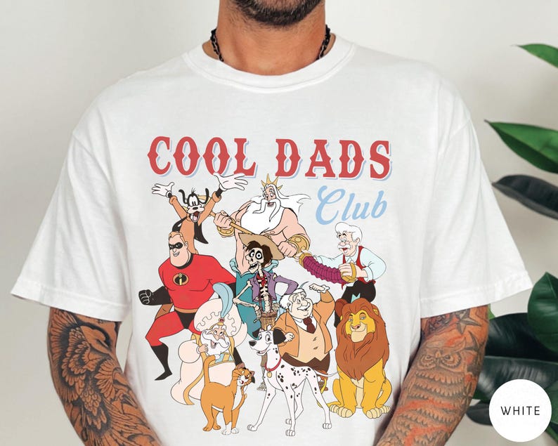 May include: White t-shirt with the text "COOL DADS Club" in red and blue. The shirt features cartoon characters including Mr. Incredible, Simba, and others. The shirt is a crew neck and has short sleeves.