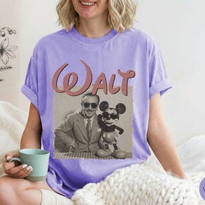 Puede incluir: Una camiseta violeta con un gr&aacute;fico vintage de Walt Disney y Mickey Mouse. El gr&aacute;fico est&aacute; en un marco rectangular con la palabra "Walt" en escritura rosa. La camiseta es de un estilo c&oacute;modo e informal.