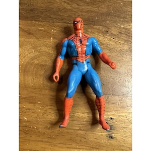 Puede incluir: Una figura de acci&oacute;n de pl&aacute;stico de un superh&eacute;roe con un traje rojo y azul que presenta un emblema de ara&ntilde;a negro en el pecho. La figura tiene una m&aacute;scara roja con parches oculares blancos, botas y guantes rojos, y torso y piernas de color azul.