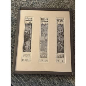 Peut inclure: Œuvre d'art encadrée avec trois panneaux verticaux : "Intégrité", "Leadership" et "Engagement". Chaque panneau présente une illustration et du texte, avec les noms "Devora", "Miriam" et "Ruth" en bas. Le cadre est gris foncé.