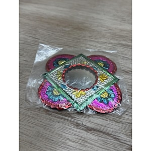 May include: A collection of colorful, decorative metallic embellishments in a clear plastic bag. The embellishments include a square frame and several circular pieces with floral patterns in shades of pink, blue, green, and yellow.