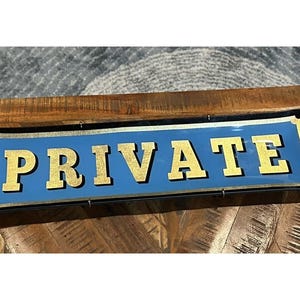 以下が含まれることがあります： 青い背景に「PRIVATE」の文字が金色で書かれた長方形の看板。黒い縁取りがあり、木製の表面に取り付けられています。装飾品です。