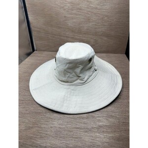 May include: A wide-brimmed bucket hat in a solid off-white color. The hat features a rounded crown, a flat brim, and two small metallic ventilation eyelets on each side of the crown. The fabric has a visible woven texture throughout the entire piece.