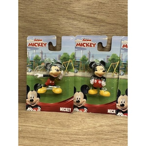Peut inclure: Plusieurs figurines de Mickey Mouse sur leur emballage d'origine. Les figurines sont dans différentes poses, portant un short rouge, des chaussures jaunes et des gants noirs. L'emballage porte les mots "Junior Mickey" et une image de dessin animé de Mickey.