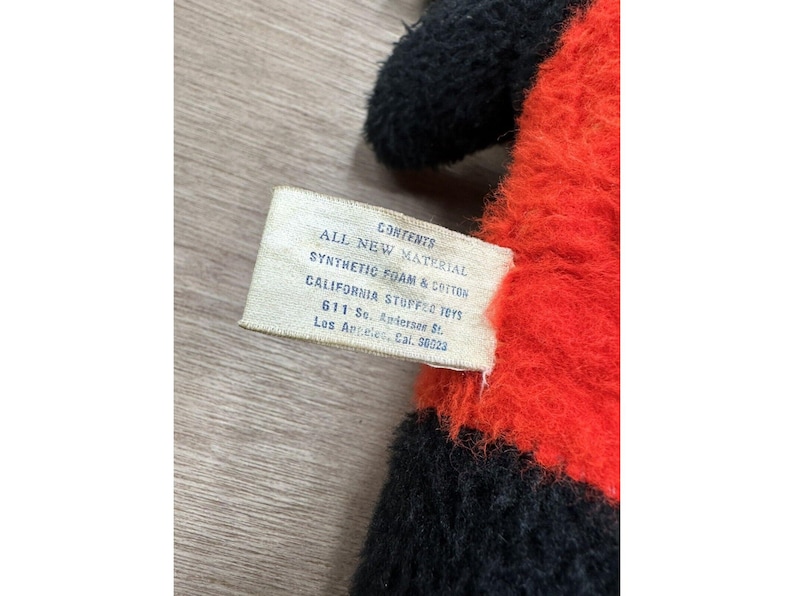 May include: Close-up of a stuffed toy with black and red fur. A tag reads "CONTENTS ALL NEW MATERIAL SYNTHETIC FOAM & COTTON CALIFORNIA STUFFED TOYS 611 So. Andersen St. Los Angeles, Cal. 90023."