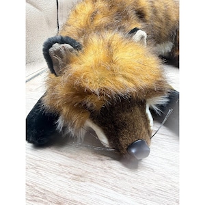 May include: A plush fox toy with brown, orange, and black fur. The fox is lying down with its head resting on a wooden surface. The toy has a black nose and black ears.
