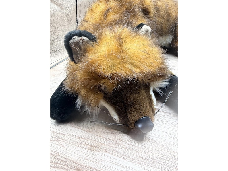 May include: A plush fox toy with brown, orange, and black fur. The fox is lying down with its head resting on a wooden surface. The toy has a black nose and black ears.