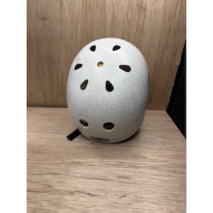 Könnte beinhalten: Ein hellgrauer, gesprenkelter Helm mit einer glatten, abgerundeten Schale, der mehrere ovale Belüftungslöcher in einem radialen Muster auf der Oberseite sowie ein kleines schwarzes Pro-Tec-Markenetikett am unteren Vorderrand aufweist.