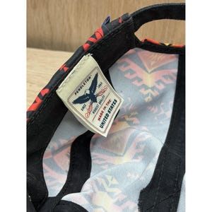 May include: A black baseball cap with a colorful geometric pattern on the interior lining. A white fabric tag is sewn inside, featuring a blue eagle graphic, the text PENDLETON SINCE 1863 HIGHEST QUALITY, and the text MADE IN THE UNITED STATES.