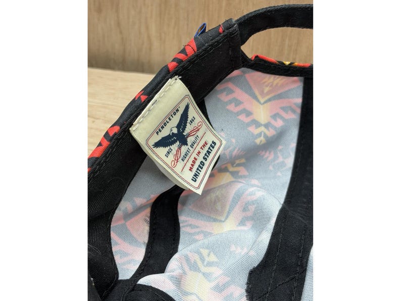 May include: A black baseball cap with a colorful geometric pattern on the interior lining. A white fabric tag is sewn inside, featuring a blue eagle graphic, the text PENDLETON SINCE 1863 HIGHEST QUALITY, and the text MADE IN THE UNITED STATES.