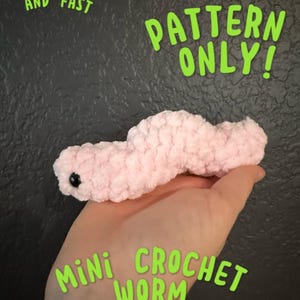 May include: A pink crocheted worm with black eyes. The worm is being held in a hand. The text "SUPER EASY AND FAST" is in the top left corner of the image. The text "PATTERN ONLY!" is in the top center of the image. The text "mini CROCHET WORM" is in the bottom center of the image.