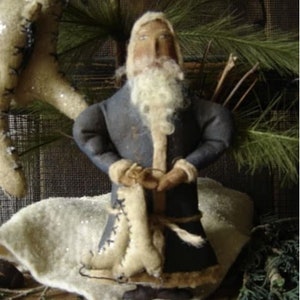 May include: A handmade felt Santa Claus doll wearing a blue coat with white fur trim. He is holding a white felt bag in his hands and has a white beard and moustache.