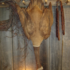 May include: A brown and white goose-shaped wall decor with a rustic wooden background. The goose is made of fabric and has a long neck and a white stripe around its neck.
