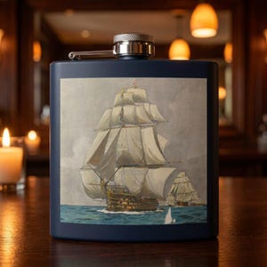 May include: A navy blue hip flask with a silver cap and a hinged top. The flask displays a watercolour painting of a tall ship at sea. The ship has white sails and is set against a grey sky.