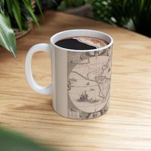 May include: White ceramic mug with a vintage world map design. The map is in shades of brown and beige and features a ship sailing on the ocean. The mug is filled with coffee.