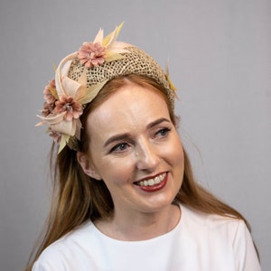 May include: A woman with long, wavy, light brown hair is wearing a white t-shirt and a headband with a beige fabric base and pink fabric flowers.