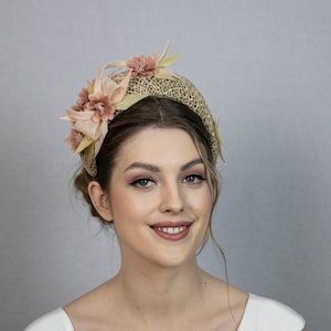 May include: A woman wearing a light brown headband with pink flowers. The headband is made of woven straw and has a wide, comfortable band.