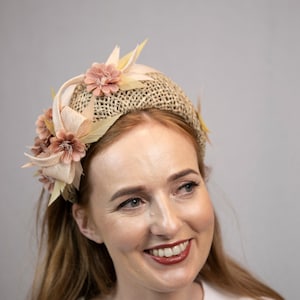 May include: A woman with long, brown hair is wearing a headband made of woven straw with pink fabric flowers and leaves.