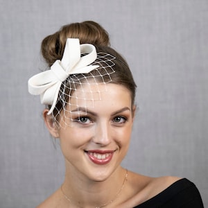 Hellelfenbein oder cremeweißer kleiner Fascinator mit Schleife, wahlweise mit Gesichtsschleier oder auch ohne. Bild 1