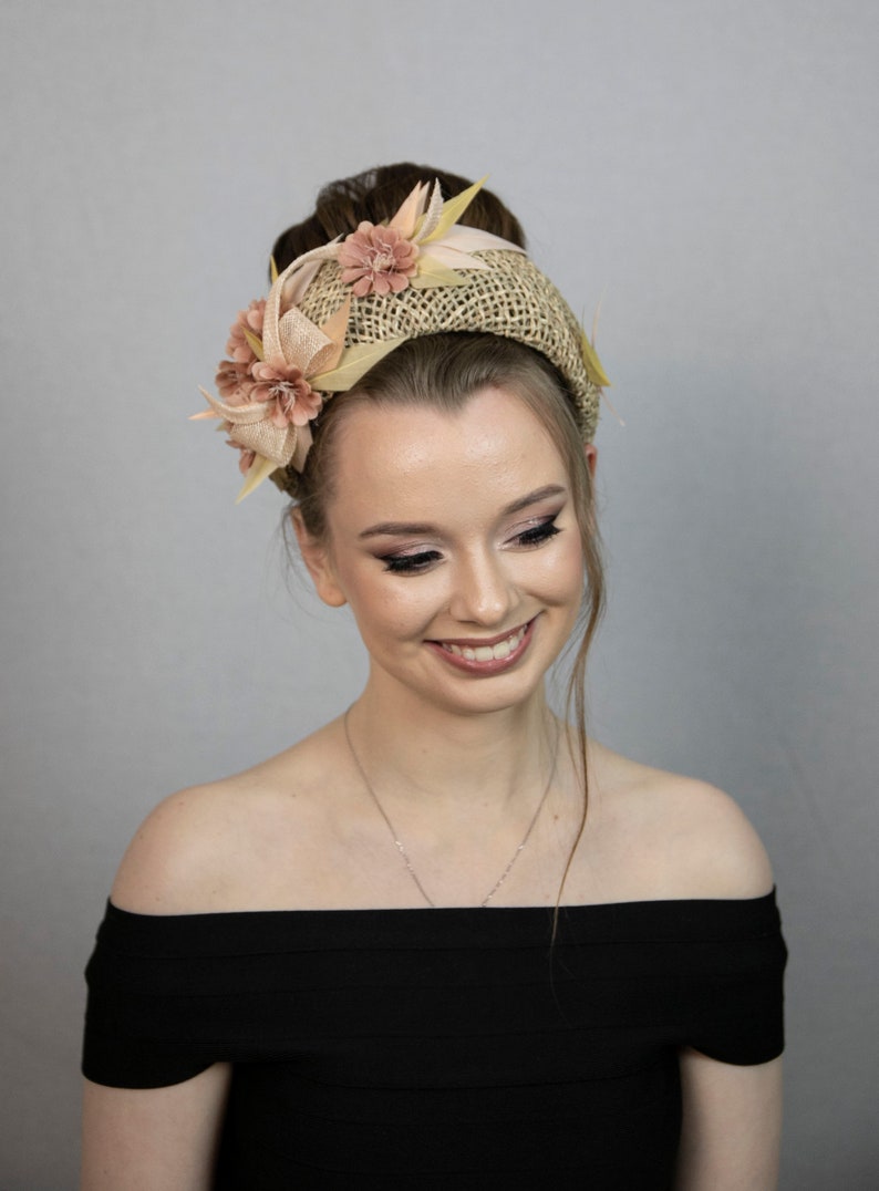 May include: A woman wearing a black off-the-shoulder dress with a straw headband adorned with pink and yellow flowers.