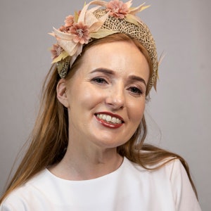 May include: A woman with long, light brown hair is wearing a white shirt and a headband with a woven base and pink fabric flowers.