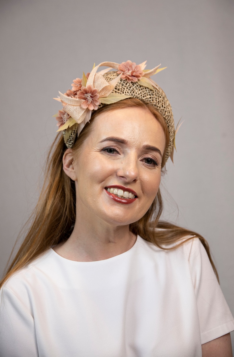 May include: A woman with long, light brown hair is wearing a white shirt and a headband with a woven base and pink fabric flowers.