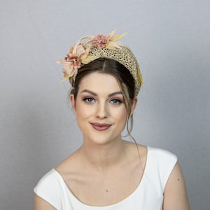May include: A woman wearing a light brown headband with a straw base and pink and yellow fabric flowers.
