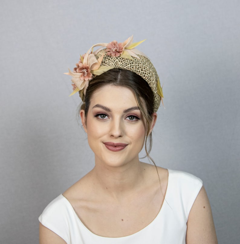 May include: A woman wearing a light brown headband with a straw base and pink and yellow fabric flowers.