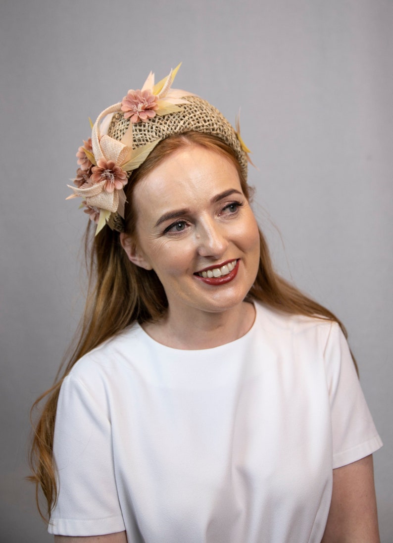May include: A woman with long, wavy, light brown hair is wearing a white t-shirt and a headband with a beige fabric base and pink fabric flowers.