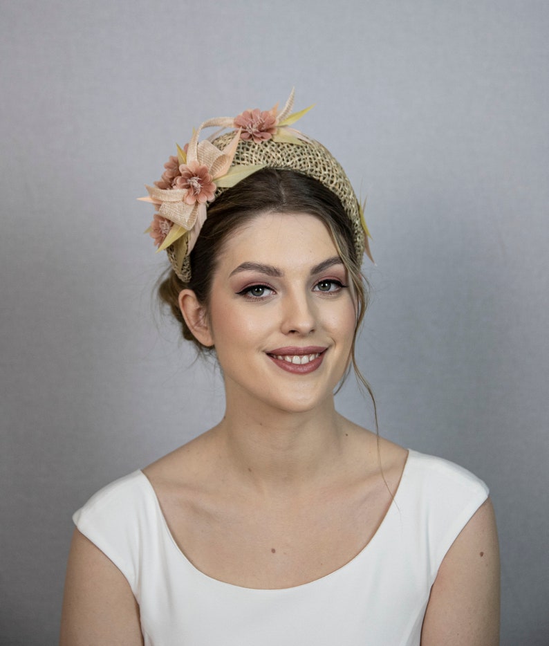May include: A woman wearing a light brown headband with pink flowers. The headband is made of woven straw and has a wide, comfortable band.