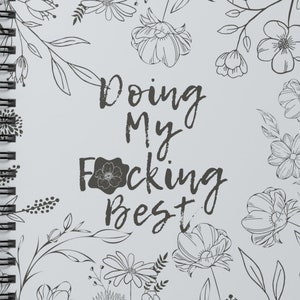 May include: A gray spiral notebook with a floral design and the text "Doing my F*cking Best" in black.