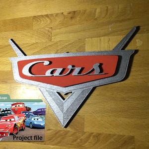 以下が含まれることがあります： 白で「Cars」の文字が入った、銀と赤のCarsロゴ。三角形のベースと上向きの2つのフィンがあります。CarsのロゴとCarsのキャラクターの画像が入ったデジタルファイルフォルダも存在します。