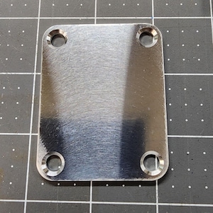 May include: A rectangular, brushed metal plate with four circular holes, one in each corner. The plate has a reflective surface and appears to be made of stainless steel. The item is likely a component or hardware piece.