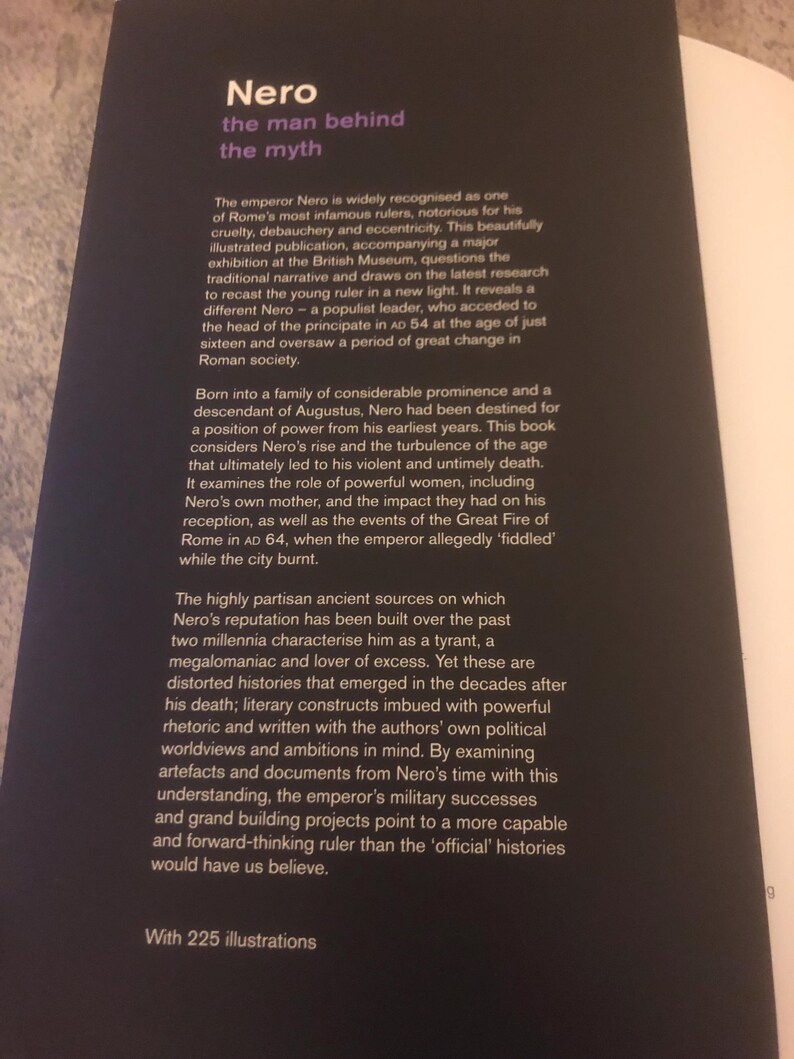 May include: Book cover with a black background and white text. The title is "Nero: The Man Behind The Myth". The text describes the book as a major exhibition at the British Museum. The book explores the life of the Roman emperor Nero, challenging traditional narratives and presenting a new perspective on his reign.