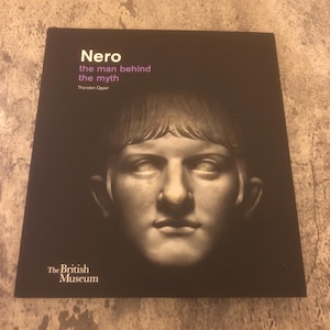 May include: A black book with the title "Nero the man behind the myth" by Thorsten Opper. The book cover features a black and white image of a bust of Nero. The book is published by The British Museum.