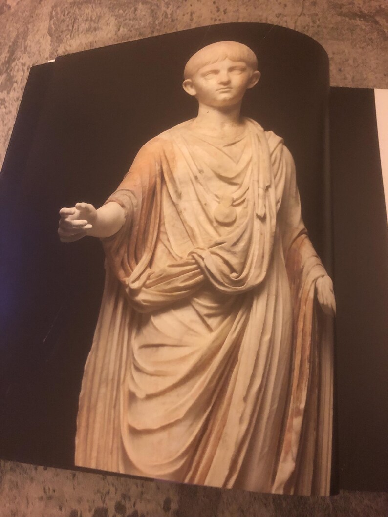 May include: A white marble statue of a young person wearing a toga. The statue is standing with one arm outstretched and the other arm bent at the elbow. The statue is set against a black background.