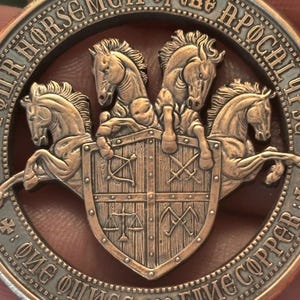 May include: A copper-colored coin featuring four horses above a shield with symbols. The coin's outer ring has the text "FOUR HORSEMEN OF THE APOCALYPSE" and "ONE OUNCE 999 FINE COPPER". The coin has a hole at the top.