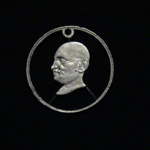 May include: A silver-toned metal pendant featuring a profile portrait of a man wearing glasses. The pendant is circular and has a smooth, polished finish.