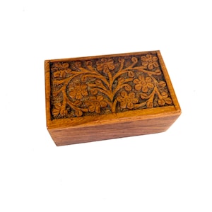 May include: A rectangular wooden box with a floral design carved into the lid. The box is made of a warm brown wood and has a simple, classic design. The floral carving is detailed and adds a decorative element to the box.