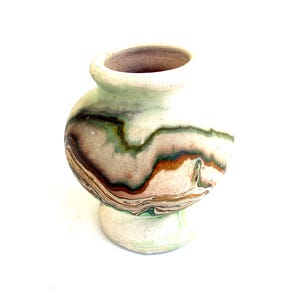 May include: A small, rounded ceramic vase with a wide, bulbous body and a narrow, flared base. The surface features a marbled, swirling pattern of earthy tones including cream, sage green, deep brown, and muted terracotta, with a smooth finish.