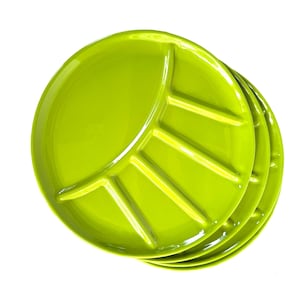 May include: A stack of three bright green ceramic plates. Each plate has a leaf-shaped design with a central section and radiating lines. The plates are round and have a glossy finish.