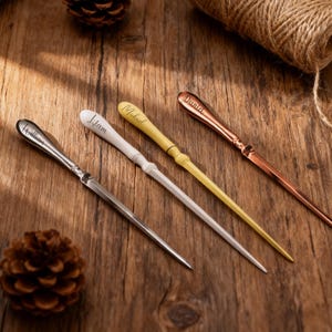 May include: Four personalized letter openers in silver, white, yellow, and copper. Each opener has a name engraved on the handle: William, Liam, Michael, and Daniel. The openers are on a wooden surface with pine cones and twine.
