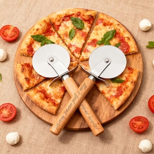 Könnte beinhalten: Zwei Pizzaschneider mit Holzgriffen, auf denen "Mom's food warms hearts!" steht, kreuzen sich über einer Pizza auf einem Holzbrett. Die Pizza ist in Scheiben geschnitten und mit Basilikum garniert. Halbierte Tomaten und Mozzarella-Kugeln sind verstreut.