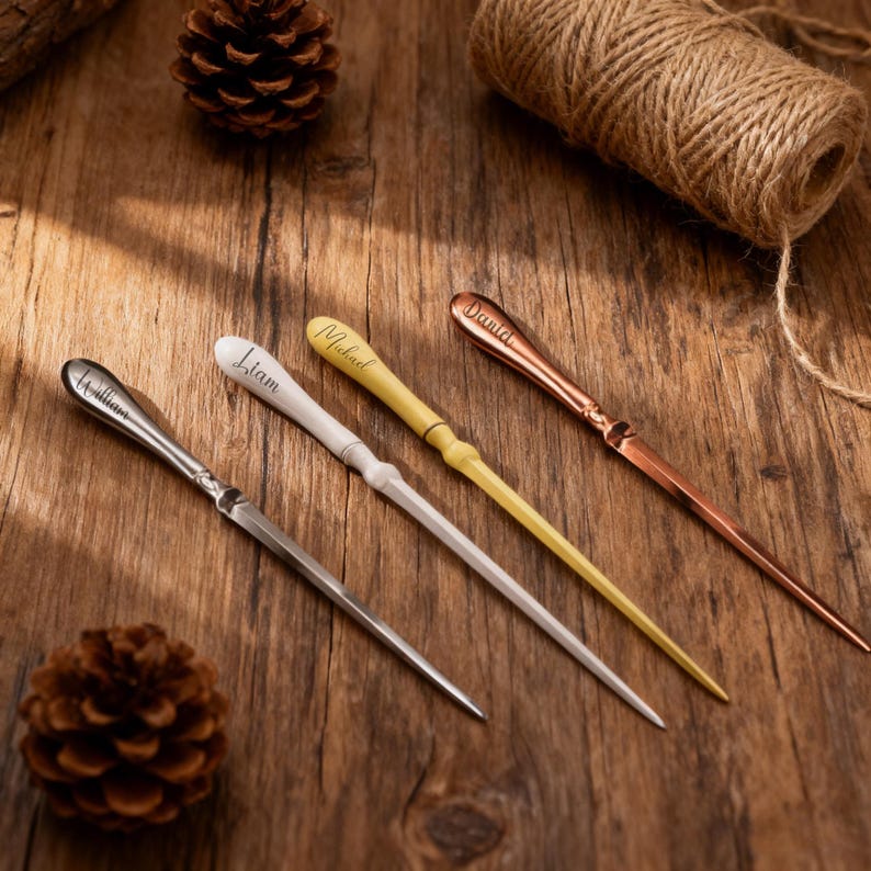 May include: Four personalized letter openers in silver, white, yellow, and copper. Each opener has a name engraved on the handle: William, Liam, Michael, and Daniel. The openers are on a wooden surface with pine cones and twine.