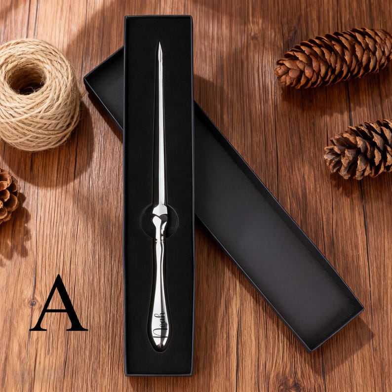 May include: A silver letter opener with a decorative handle, presented in a black gift box. The handle features a heart-shaped design and the name "Noah" is engraved on the handle. The opener is displayed on a wooden surface.