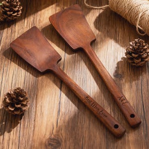 May include: Two wooden spatulas with long handles and wide, flat heads. One spatula is engraved with "Best Men Ever", the other with "A&E". The spatulas are a rich brown color and have a hole at the end of the handle.