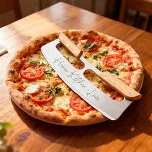 Könnte beinhalten: Eine frisch gebackene Pizza mit Tomatenscheiben, Mozzarella und Basilikum. Ein Pizzaschneider aus Edelstahl mit Holzgriffen liegt obenauf. Auf dem Schneider steht der Text "Home. Kitchen = Love".