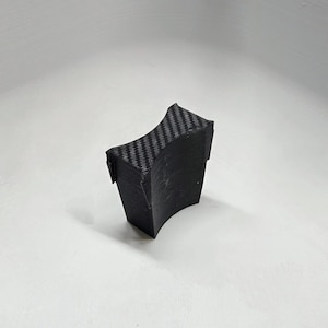 May include: A black plastic car phone holder with a carbon fiber pattern. The holder is designed to fit in a cup holder.